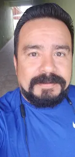 A man in a blue athletic shirt in a hallway.