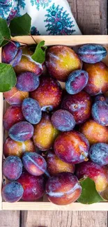 Mobile wallpaper with colorful plums in a wooden crate.