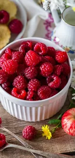 Fresh raspberries in a bowl on a rustic table with flowers and apples.