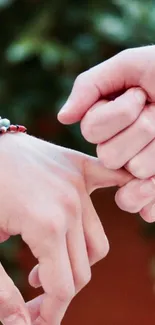 Two hands linked in a pinky promise against a blurred background.