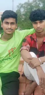 Two friends posing in a serene outdoor setting with greenery in the background.