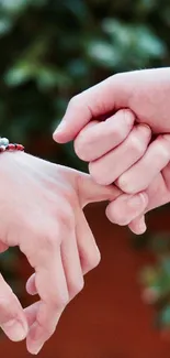 Two hands linked by colorful bracelets in front of a green background.