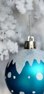 Frosty blue Christmas ornament hanging on snowy branches.