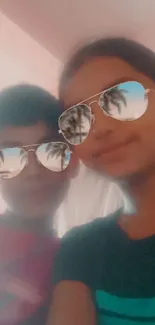 Two kids wearing sunglasses with palm tree reflections.