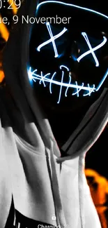 Figure with neon mask in black hoodie on dark background.