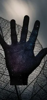 Silhouetted hand with galaxy motif on leaf background.