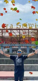 Man joyfully posing at Gelora Sriwijaya Stadium entrance under blue sky.