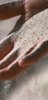 Hand releasing sand in a calming mobile wallpaper scene.