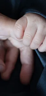 Parent hand gently holding baby's hand on a dark gray background.