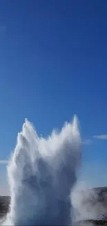 Vibrant geyser eruption under clear blue sky.