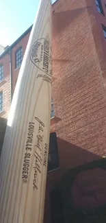 Giant baseball bat against a red brick building in cityscape.