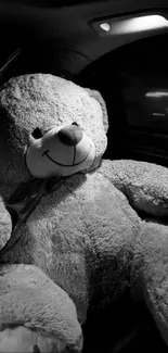 Black and white image of a giant teddy bear in a car seat.