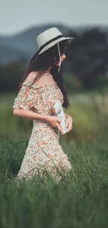 Woman in a floral dress with a straw hat, standing in a grassy field.