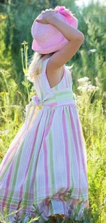 Girl in a striped dress and hat in a sunny meadow.