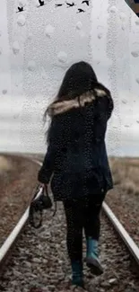 A girl in a coat walks on railway tracks in the rain.