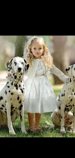 Girl in white dress with two Dalmatians sitting on grass.