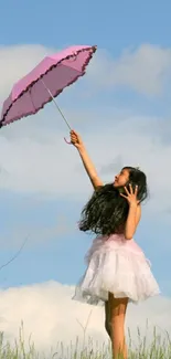 Girl with pink umbrella under blue sky on a grassy field.