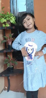 Smiling girl in blue dress with plants on shelf.