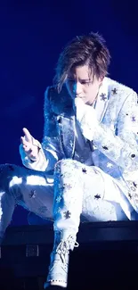 Charismatic performer in white suit on stage with deep blue lighting.