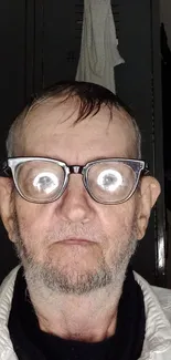 Portrait with glasses reflecting light on a muted gray background.