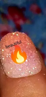 Glittery gradient nail art with a fire emoji on a blue floral background.