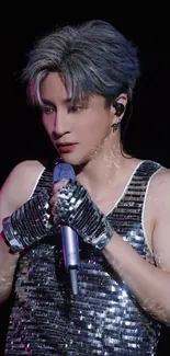 Performer in glittering silver attire holding a microphone on stage.