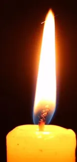 A glowing candle flame against a dark background for a mobile wallpaper.