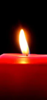 Red candle with glowing flame on a dark background.