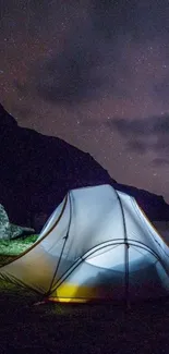 Glowing tent under a starry night sky with mountains in the background.