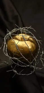 Golden apple wrapped in barbed wire on a dark fabric.