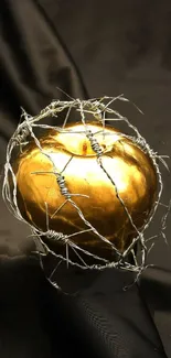 Golden apple wrapped in barbed wire on dark fabric background.