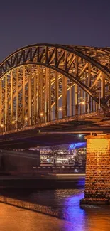 Golden-lit bridge at night with reflection on river.