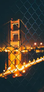 Golden Gate Bridge at night through a fence, glowing with city lights.