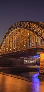 Golden-lit bridge over water at night with reflections.