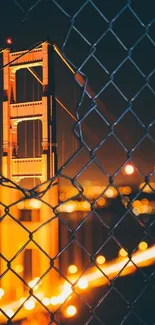 Golden Gate Bridge at night through a chain-link fence, warmly illuminated.