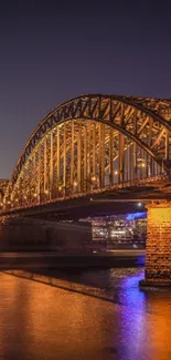 Golden bridge at night with reflections on the water under a clear sky.