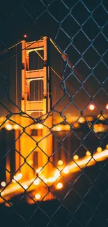 Golden bridge glowing in the night through chain-link fence.