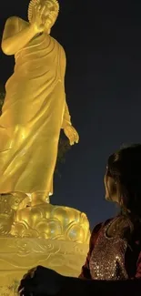 Golden Buddha statue illuminated at night with a gazing figure.