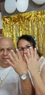 Two people celebrating with gold backdrop and rings displayed.