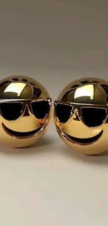 Two golden emoji spheres wearing sunglasses with smiles.