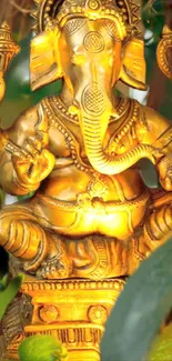 Golden Ganesha statue with lush green background for phone wallpaper.