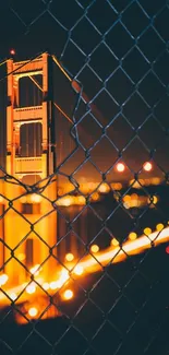 Golden Gate Bridge at night seen through a fence with glowing lights.