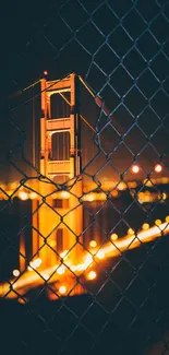 Golden Gate Bridge illuminated at night through a wire fence.