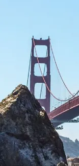 Golden Gate Bridge over blue sky with rocky foreground.