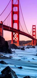 Golden Gate Bridge at sunset with purple sky and rocky shore.