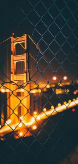 Golden Gate Bridge at night with vibrant lights viewed through fence.