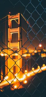 Golden Gate Bridge glowing at night through chain-link fence.