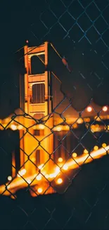 Golden Gate Bridge glowing at night through fence.