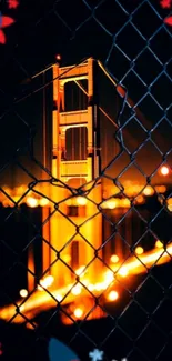 Golden Gate Bridge glowing at night through a chain-link fence.