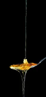 Golden honey dripping from a spoon against a black background.